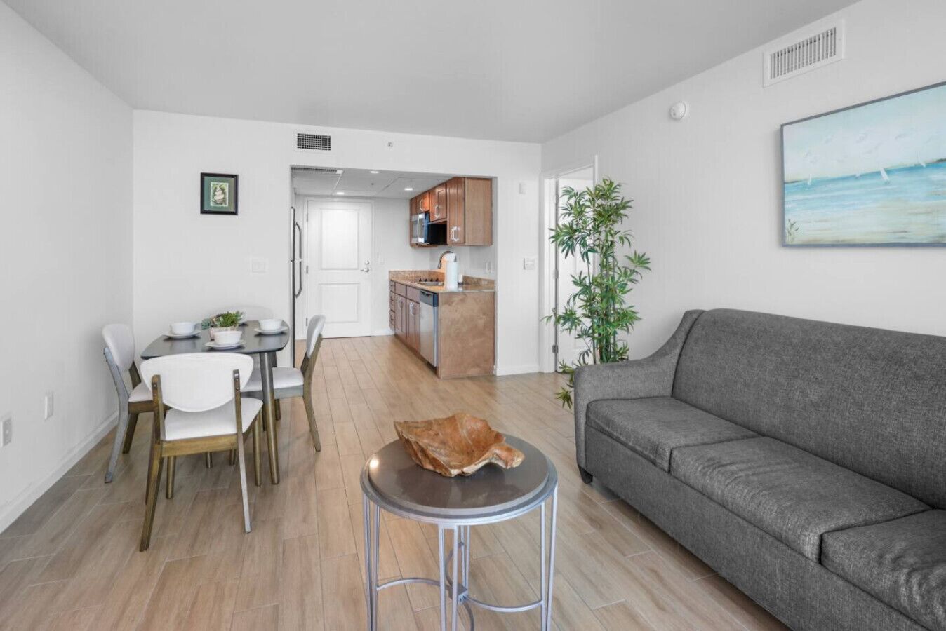 Una sala de estar moderna con un sofá gris, un comedor con mesa y sillas, una cocina con armarios de madera y un ventanal con vistas.
