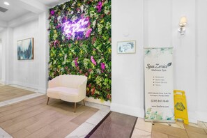 Un espace d’accueil avec un canapé blanc, un panneau lumineux au néon, un mur végétal et une affiche du centre de bien-être SpaZeria.