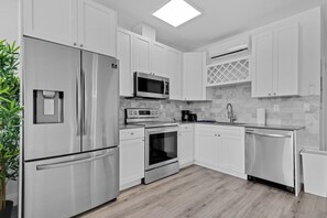 Una cocina moderna con armarios blancos, electrodomésticos de acero inoxidable, un microondas, horno y un lavamanos.
