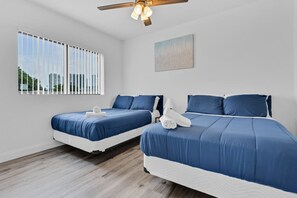 A hotel room with two beds, a ceiling fan, a window with blinds, and a painting on the wall. - Modern Stay near Design District (Miami)