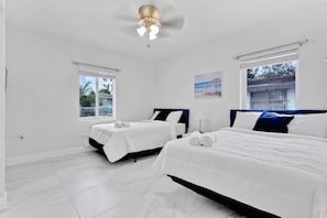 A hotel room with two beds, a ceiling fan, a window with a view of the outside, and a painting on the wall. - Cozy Caribbean Retreat Near Wynwood & Design (Miami)