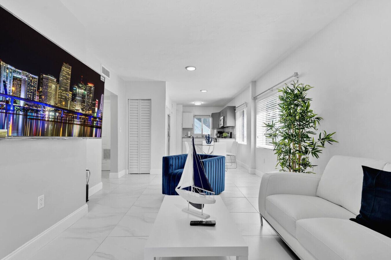 A modern living room with a white sofa, a blue chair, a sailboat model, and a cityscape mural on the wall.