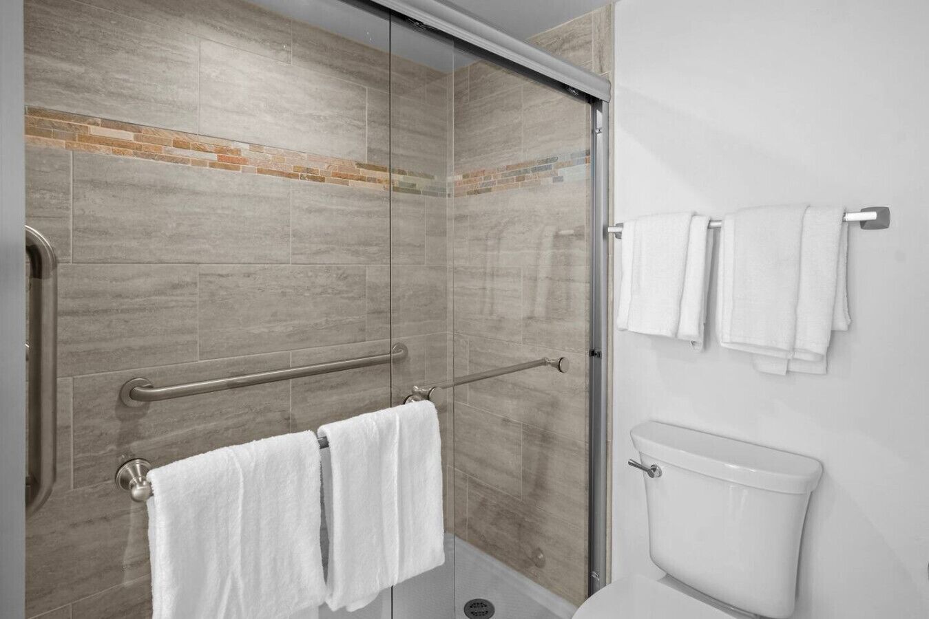 Une douche avec une porte en verre, une barre d’appui et un porte-serviettes avec des serviettes.