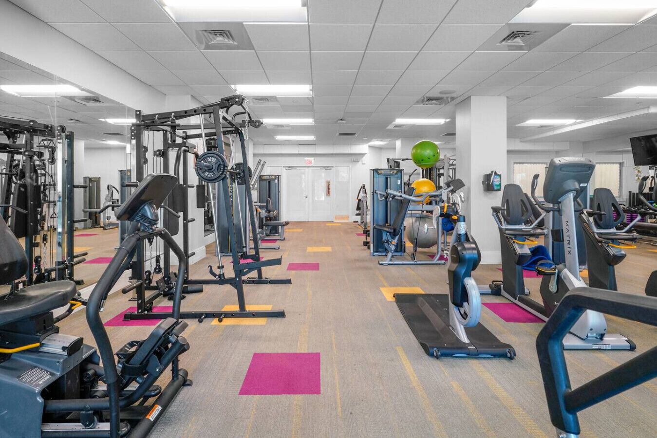 Een sportschool met diverse fitnessapparaten, een groene fitnessbal en een loopband.