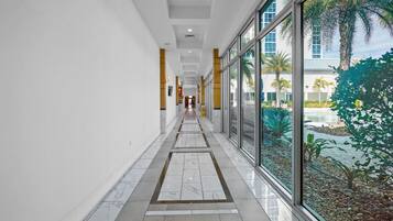 A corridor with marble flooring, large windows, and a view of a pool and palm trees.