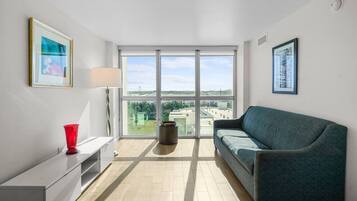 A modern living room with a sofa, a red vase, a lamp, and a large window offering a view of the city.