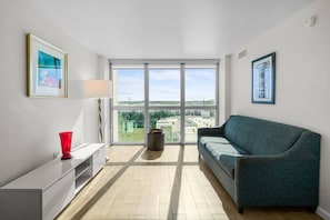 Ein modernes Wohnzimmer mit einer Couch, einer roten Vase, einer Lampe und einem großen Fenster mit Blick auf die Stadt.