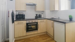 A compact kitchen with wooden cabinets, a microwave, a coffee maker, and a sink. - Devon Seaside Apartment (Paignton)