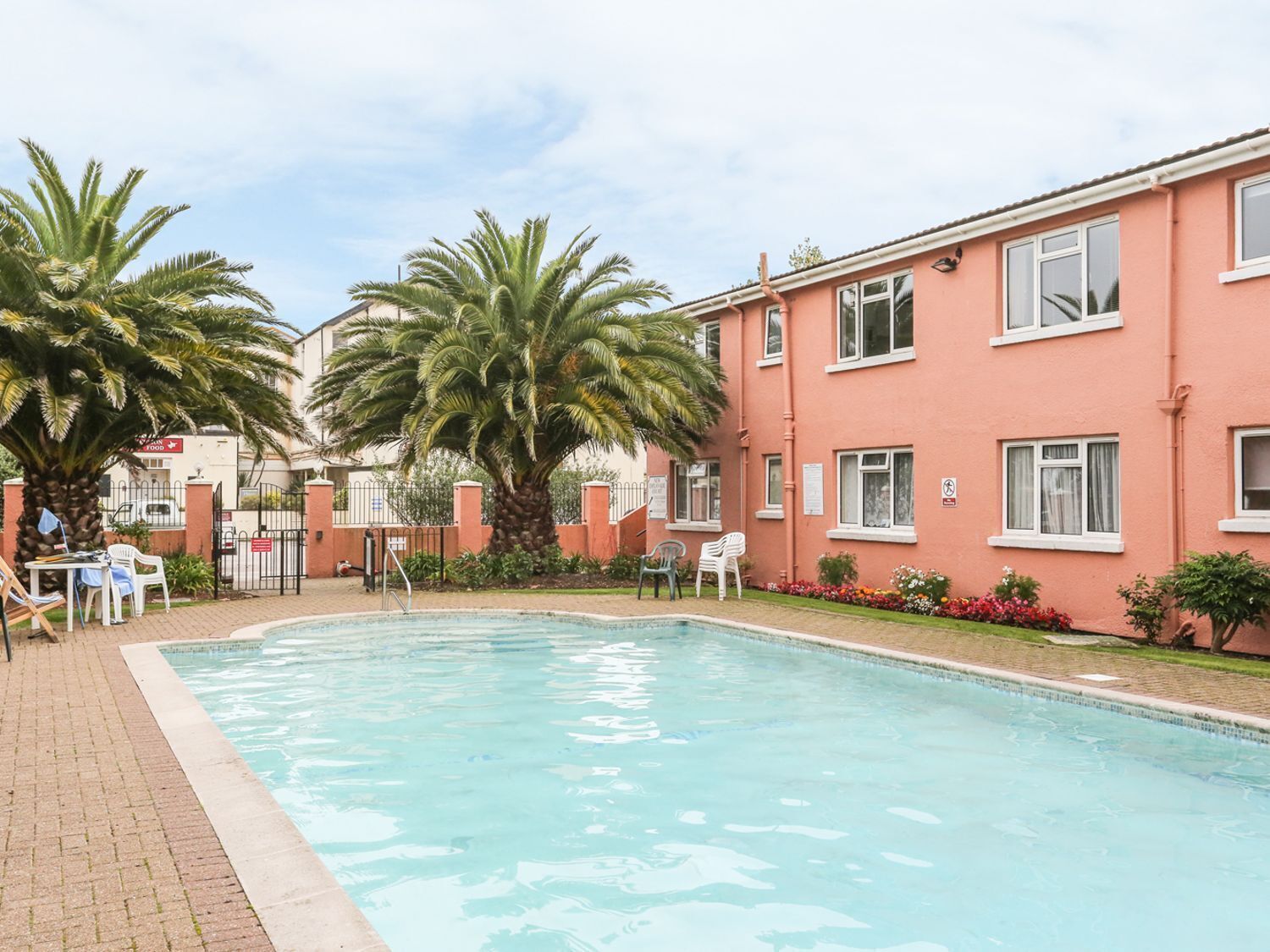 A swimming pool with palm trees, a brick patio, and a building with multiple windows.