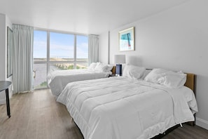 A hotel room with two beds, a view of a body of water, a framed picture on the wall, and a lamp on the nightstand. - Modern Cozy Apartment in Downtown Fort Myers (Fort Myers)