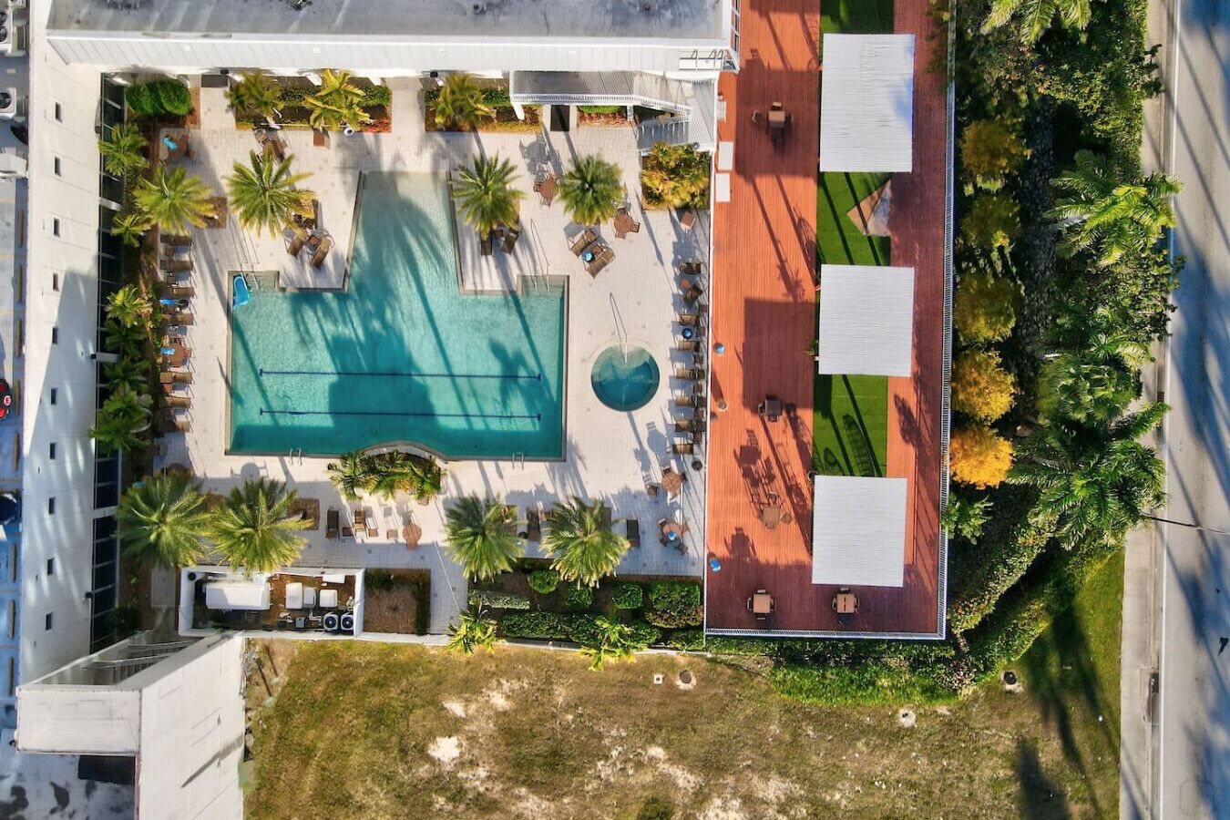 Vista aèria d'un hotel amb piscina, gandules, palmeres i una pista de tennis.
