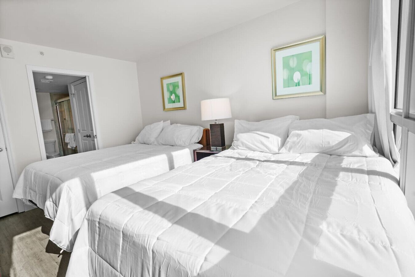 Een hotelkamer met twee bedden, een nachtkastje, een lamp en twee ingelijste foto’s aan de muur.