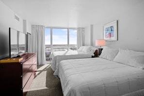 Ein Hotelzimmer mit zwei Betten, einem Fernseher, einem Schreibtisch und einem Fenster mit Blick auf die Stadt.