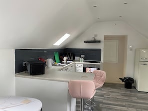 A compact kitchen with a bar area, a refrigerator, and a trash bin. - The Cottage (Middlesbrough)