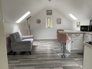 A modern loft bedroom with a sloped ceiling, a large window, a built-in desk, and a kitchenette. - The Cottage (Middlesbrough)