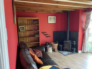 A living room with a red wall, a black sofa, a wooden bookshelf, a fireplace, and a window with curtains. - The Cottage (Middlesbrough)