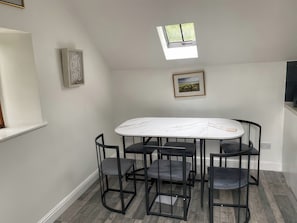 A dining area with a white marble table and black metal chairs, a skylight, and framed artwork on the walls. - The Cottage (Middlesbrough)