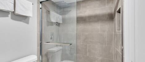 A modern bathroom with a glass-enclosed shower, a toilet, and a sink.