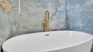 Un bagno con una vasca freestanding, pareti in marmo e un rubinetto dorato.
