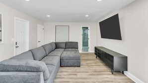 A modern living room with a sectional sofa, a flat-screen TV, and a minimalist design. - Penthouse Suite Steps to the Beach | Jersey Shore Stay (Seaside Heights)