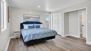 Un dormitorio con cama, mesitas de noche, un cuadro y una puerta.