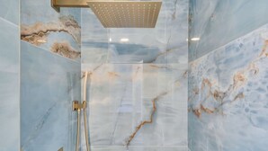 Un baño con ducha, paredes de mármol y un cabezal de ducha dorado.