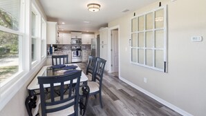 A kitchen with white cabinets, a dining table with chairs, and a large window. - Backwater Bungalow Sleeps 8 Kayaks+ Dock+ Fire Pit (Crystal River)