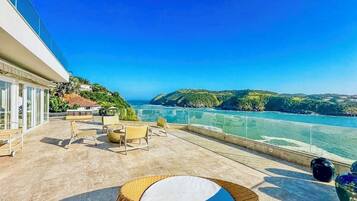 Una terraza con asientos al aire libre, vista al mar y un edificio con grandes ventanales.