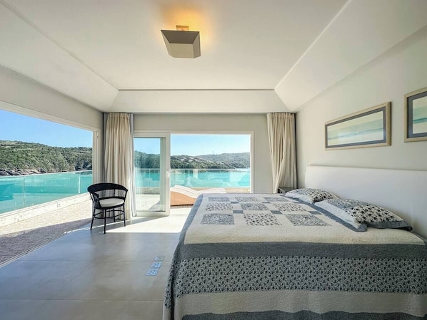 Un dormitorio con una cama grande, una silla y un balcón con vistas al mar.