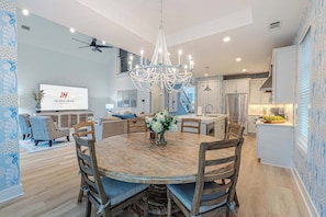 A modern kitchen with a chandelier, dining area with wooden table and chairs, and a living room with a sofa and TV. - Luxury Dunes Paradise - Private Pool (Hilton Head Island)