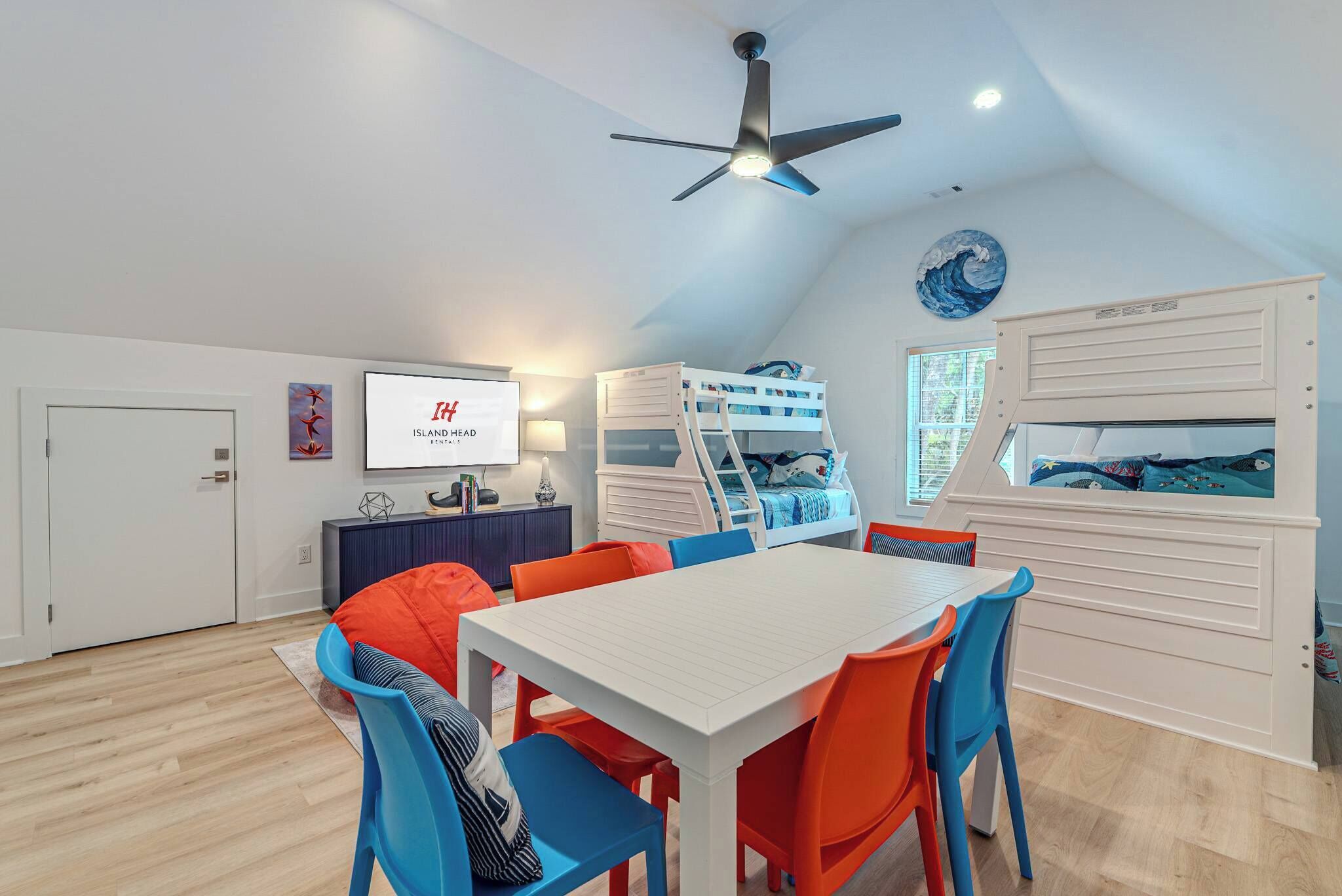 A room with a bunk bed, a dining table with chairs, a ceiling fan, and a wall-mounted TV.