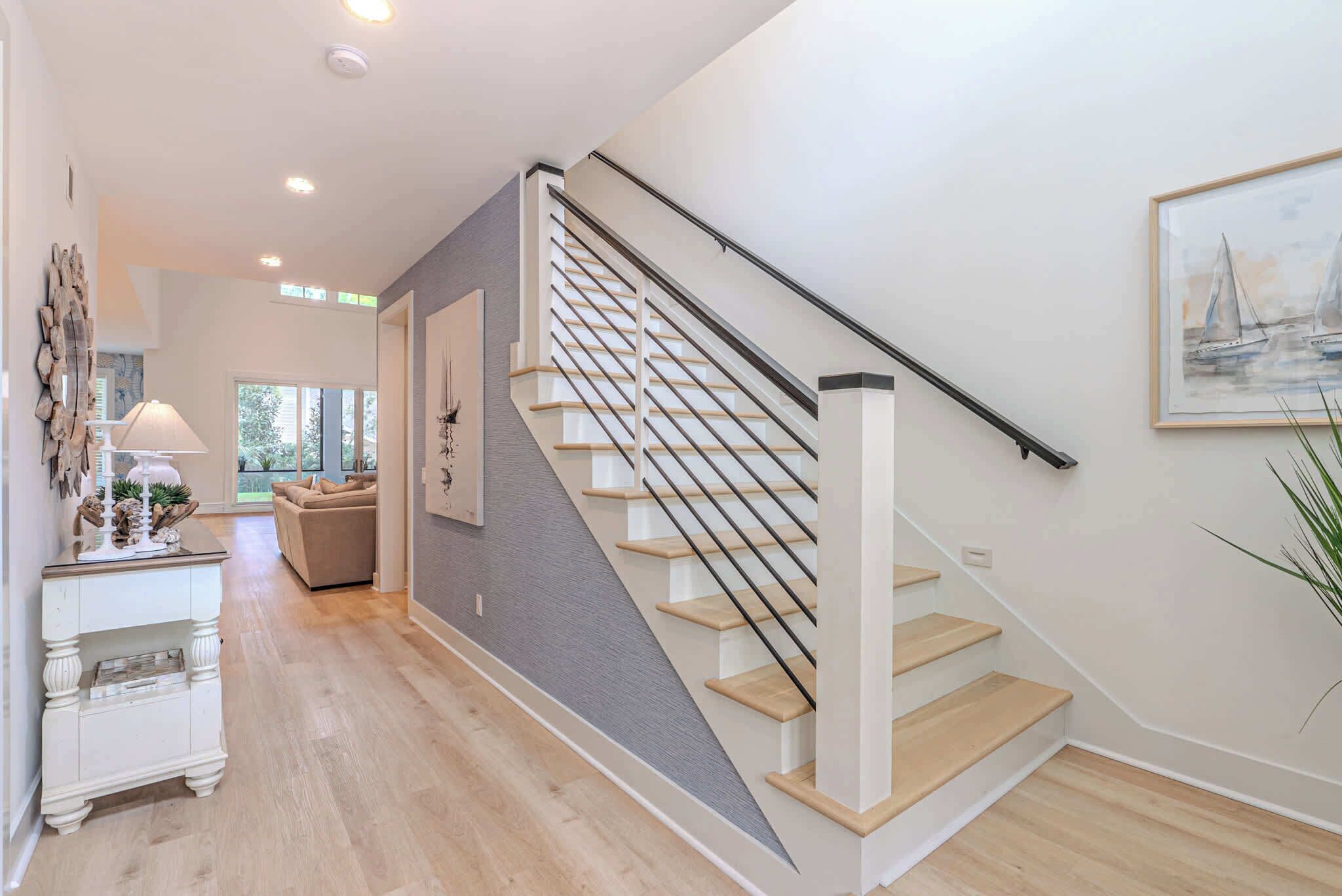 Een trap met houten treden en een metalen leuning, een witte console tafel met decoratieve objecten, een beige bank en een lijst met een schilderij aan de muur.