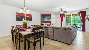 A dining area with a wooden table and chairs, a sofa, and a ceiling fan. - Wishes Villa Pool & Hot Tub (Kissimmee)