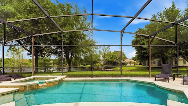 A covered outdoor swimming pool with a view of a green landscape and trees. - Wishes Villa Pool & Hot Tub (Kissimmee)