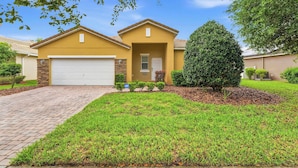A residential house with a garage, a well-maintained lawn, and a large tree. - Wishes Villa Pool & Hot Tub (Kissimmee)