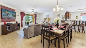 A dining area with a table set for four, a sofa, a TV, and a ceiling fan. - Wishes Villa Pool & Hot Tub (Kissimmee)