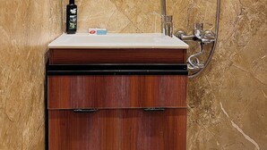 A bathroom with a marble wall, a wooden vanity with a sink, a mirror, and a shower. - Perfect studio with AC in charming 6 October city (6 October)