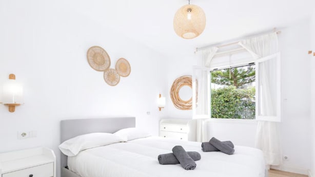 A bedroom with a bed, bedside tables, a window with curtains, and wall decor. - Nuria Cala Blanca (Cala Blanca)