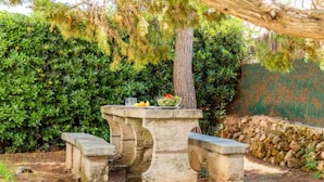 A stone bench with a table in a garden area. - Nuria Cala Blanca (Cala Blanca)