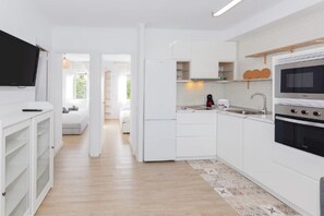 Una cucina moderna con mobili bianchi, forno integrato e televisore sopra il bancone.