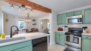Une cuisine avec des meubles de couleur turquoise, un îlot central, un lave-vaisselle, une cuisinière et un four à micro-ondes.