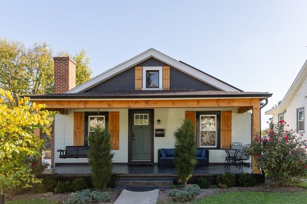 A two-story house with a front porch, a chimney, and a small garden.