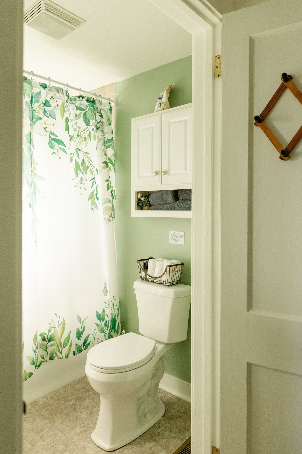 Une salle de bain avec des toilettes, un rideau de douche orné d’un motif de feuilles et un meuble au-dessus des toilettes.