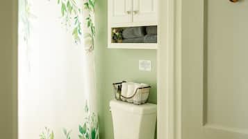 Une salle de bain avec des toilettes, un rideau de douche orné d’un motif de feuilles et un meuble au-dessus des toilettes.