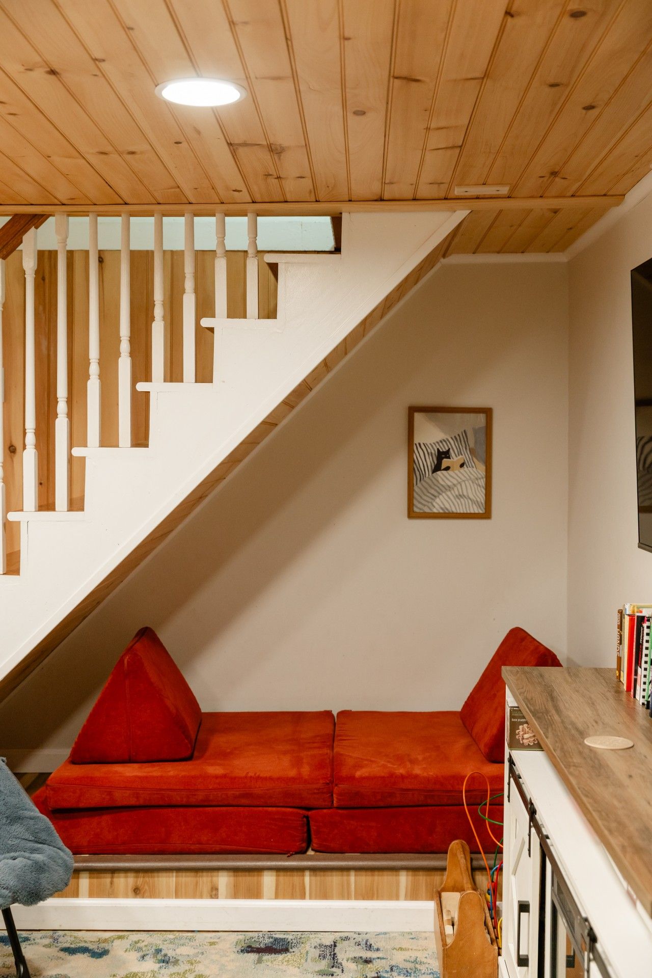 Una habitación con techo de madera, techo inclinado, un sofá rojo, un cuadro enmarcado y una mesa de madera con libros.