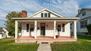 Une maison à deux étages avec un porche à l’avant, une cheminée et une pelouse bien entretenue.
