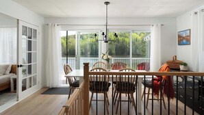 Ein Essbereich mit Holztisch und Stühlen, einer Kristallleuchter und Blick auf Grün durch große Fenster.