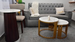 A grey sofa with a white throw blanket, two round tables with marble tops, and a dark wooden side table. - AJ Urban Escape (Nairobi)