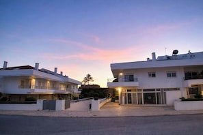A modern two-story building with a flat roof, large windows, and a paved entrance area.