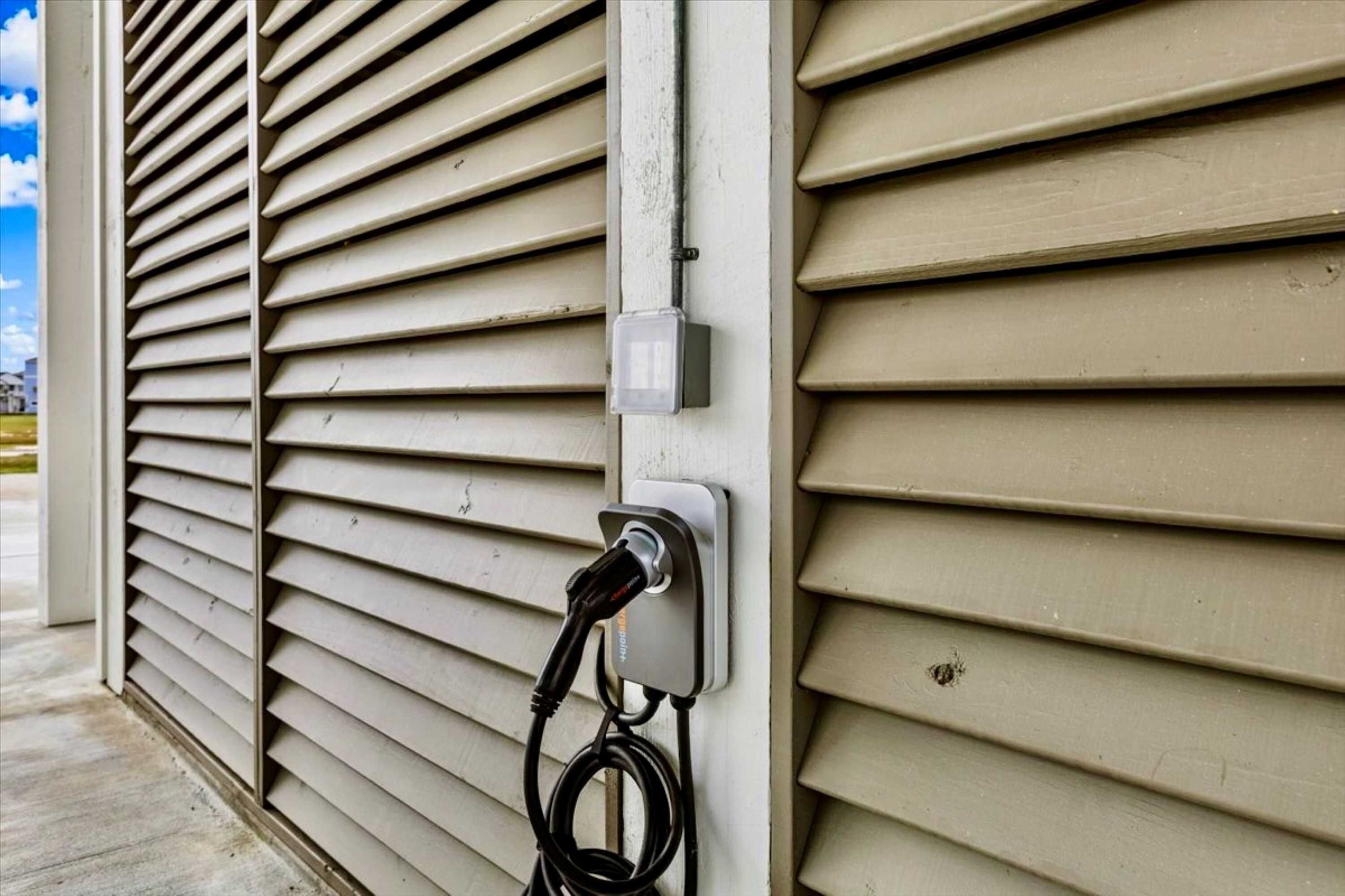 Presta d'electricitat amb un cable de càrrega connectat, fixada a una paret amb revestiment horitzontal.